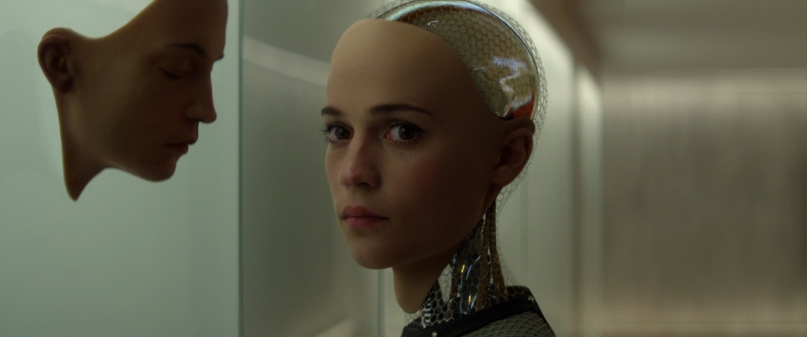 Androide humanoide de Ex Machina observa uma face artificial ao lado, enquanto partes mecânicas de sua cabeça e pescoço permanecem visíveis.