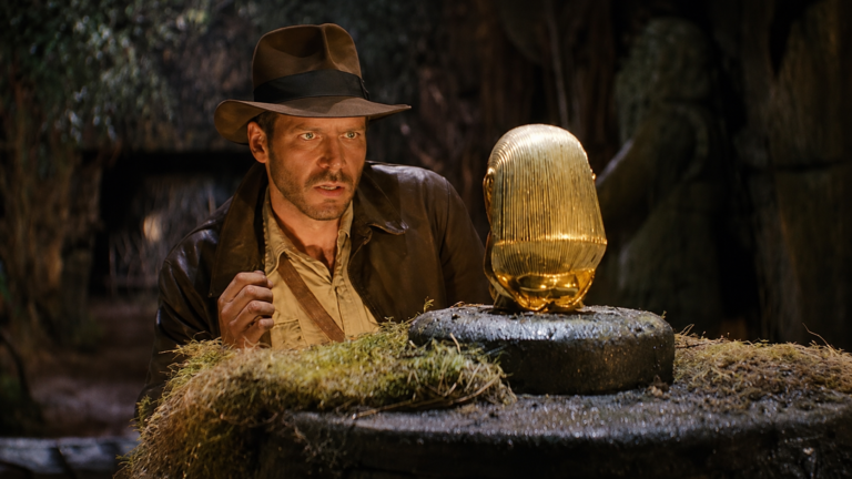 Indiana Jones observa o Ídolo Dourado sobre um pedestal de pedra dentro de um templo antigo.