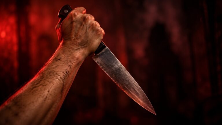 Mão segurando uma faca sob iluminação vermelha intensa, com fundo escuro e sombras desfocadas, em composição inspirada no cinema slasher.